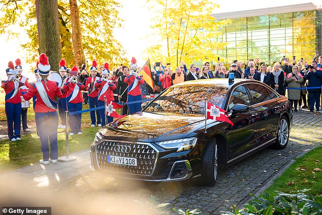 Датская королевская чета прибыла на затемненном Audi, украшенном датскими флагами, в то время как марширующий оркестр, одетый в красное, белое и синее, играл, приветствуя их.